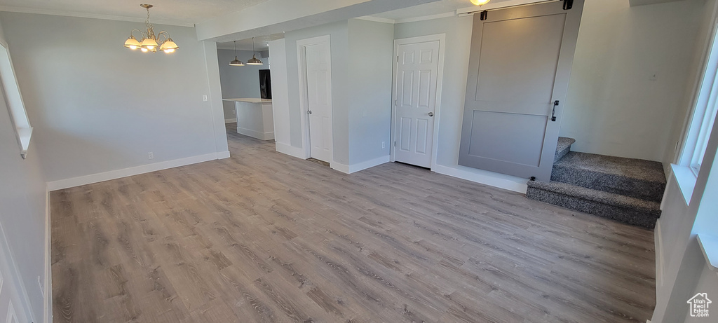 Empty room featuring ornamental molding, wood finished floors, a chandelier, stairway, and baseboards