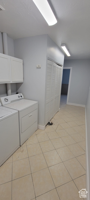 Washroom featuring cabinet space, washer and clothes dryer, baseboards, and light tile patterned floors