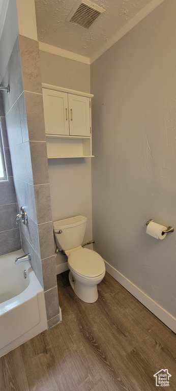 Bathroom with wood finished floors, toilet, shower / bath combination, baseboards, and a textured ceiling
