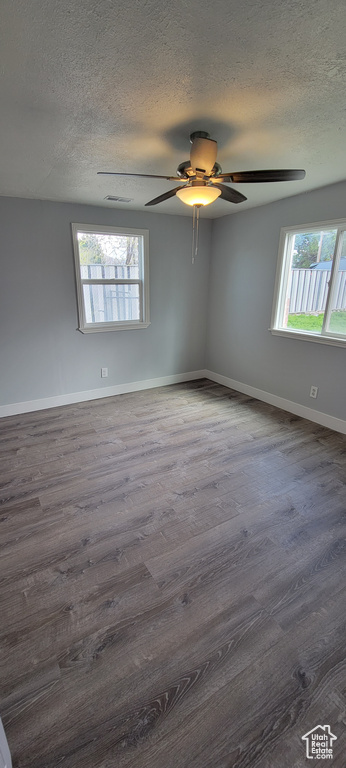 Empty room with plenty of natural light, ceiling fan, dark wood-type flooring, baseboards, and a textured ceiling