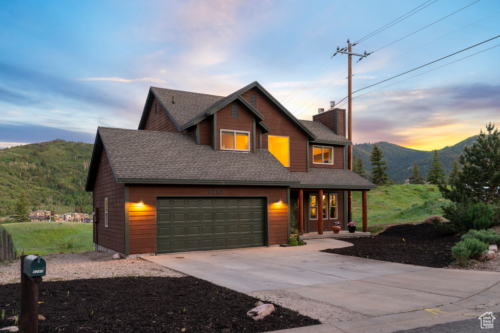 View of front of property featuring covered porch, a mountain view, a chimney, concrete driveway, and roof with shingles