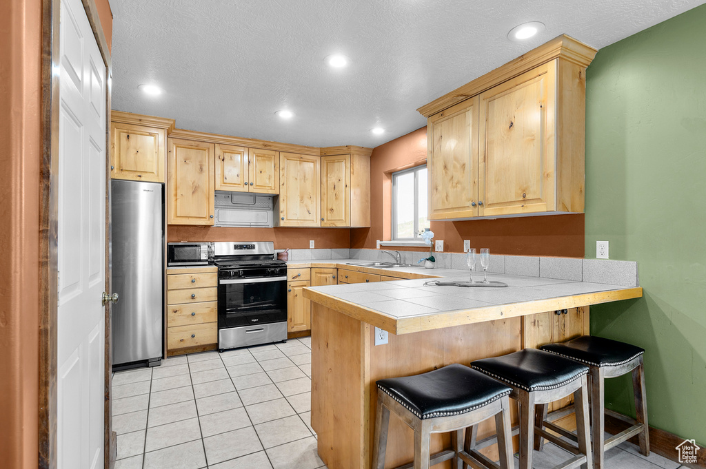 Kitchen with appliances with stainless steel finishes, light brown cabinetry, a peninsula, a sink, and a breakfast bar