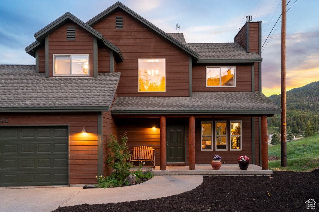 View of front of home featuring covered porch, roof with shingles, a chimney, and a garage