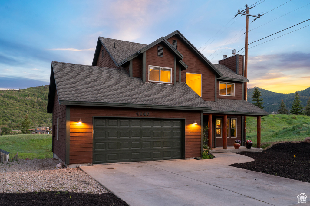 View of front of home with covered porch, a mountain view, roof with shingles, driveway, and a garage