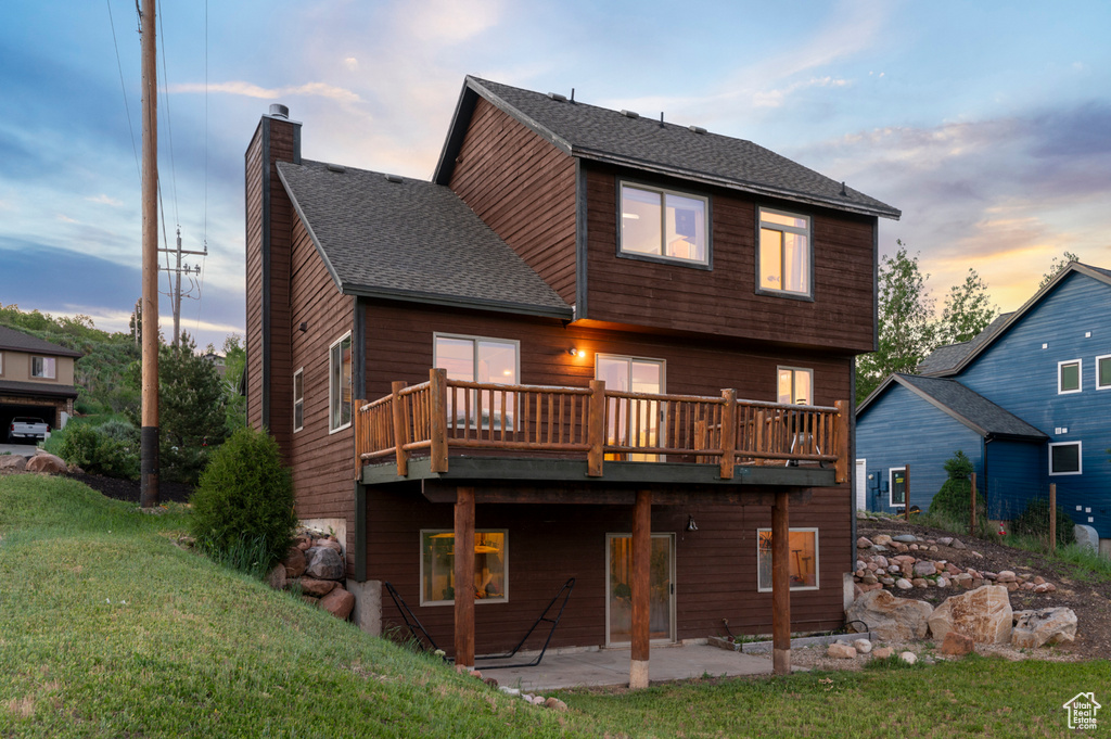 Rear view of house featuring a chimney, a deck, a yard, a shingled roof, and a patio area