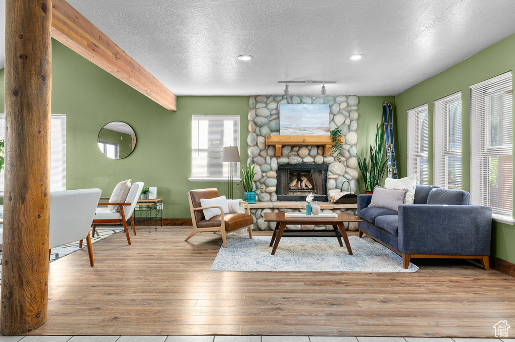 Living area with hardwood / wood-style floors, baseboards, a textured ceiling, a stone fireplace, and track lighting