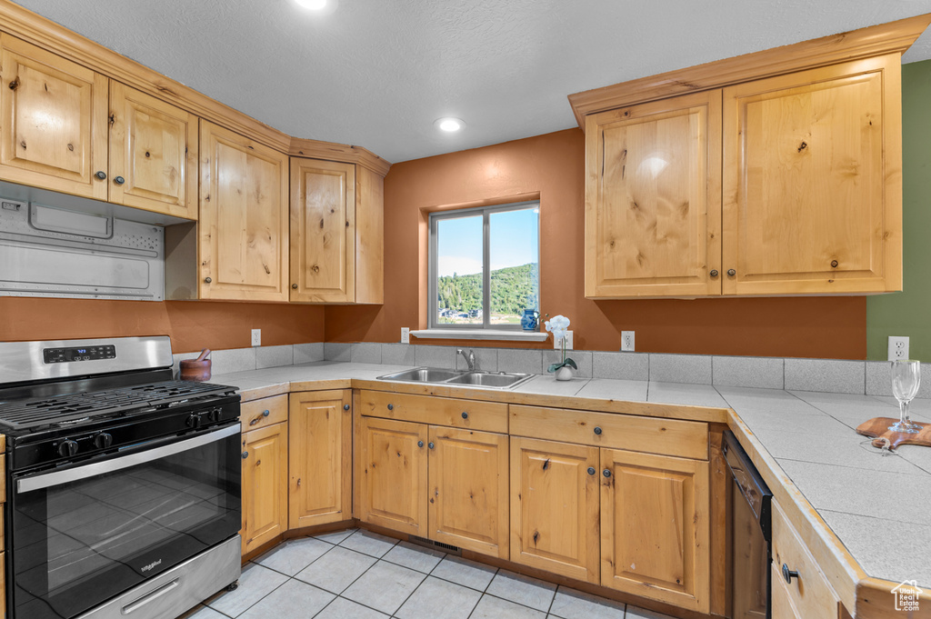 Kitchen featuring gas stove, a sink, light brown cabinets, dishwashing machine, and tile countertops