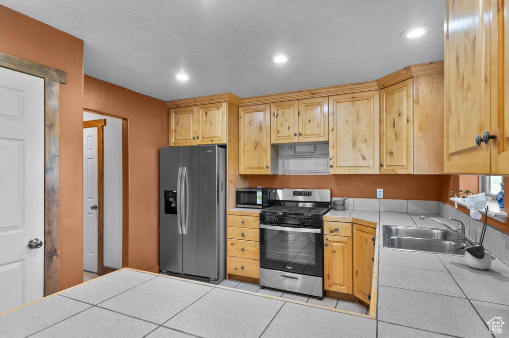 Kitchen featuring appliances with stainless steel finishes, tile counters, a sink, recessed lighting, and light brown cabinetry