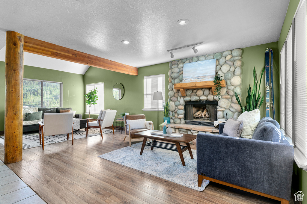 Living area featuring wood finished floors, a textured ceiling, beamed ceiling, and a stone fireplace