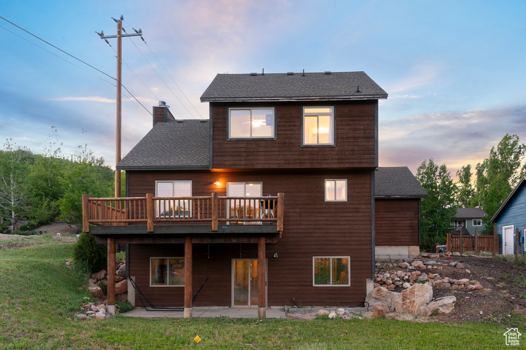 Back of house with a chimney, a wooden deck, a patio area, a shingled roof, and a lawn