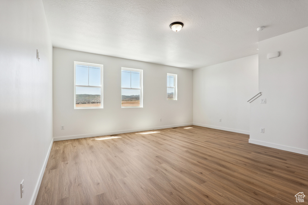 Empty room with light wood-style floors, baseboards, a textured ceiling, and a smoke detector
