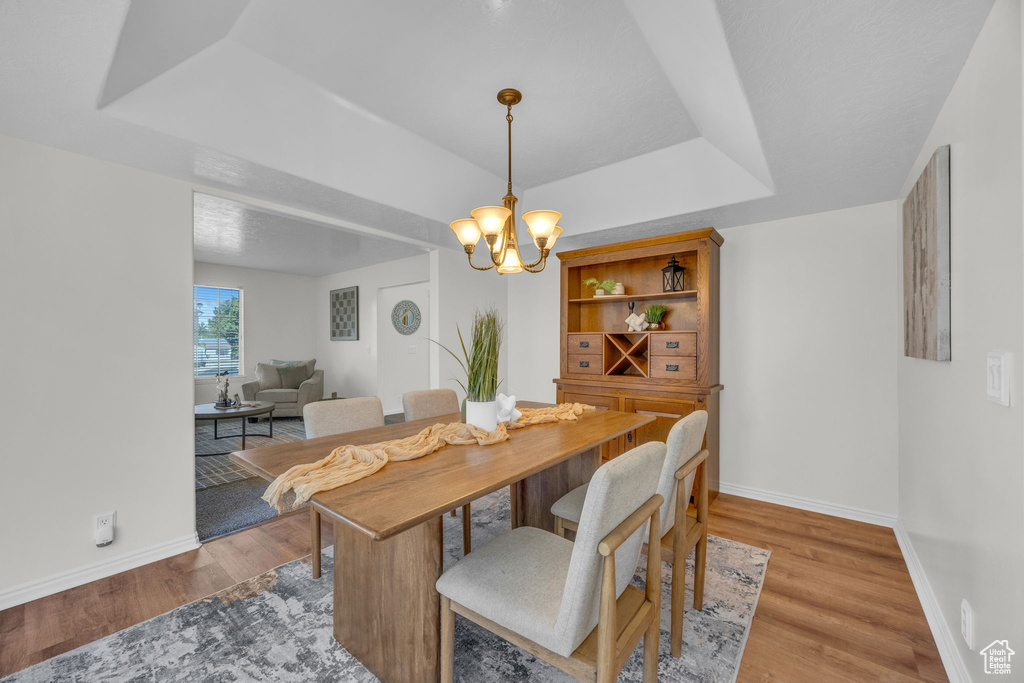Dining space with a chandelier, light wood-style flooring, a raised ceiling, and baseboards