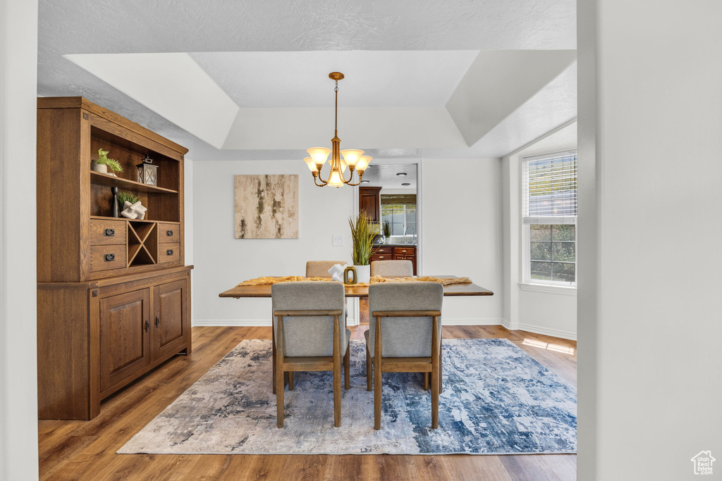 Dining area with a raised ceiling, a chandelier, wood finished floors, and baseboards