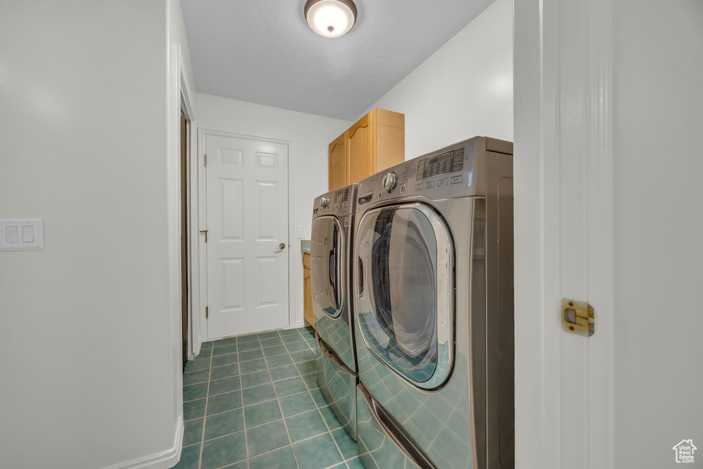 Washroom featuring separate washer and dryer, dark tile patterned floors, and cabinet space