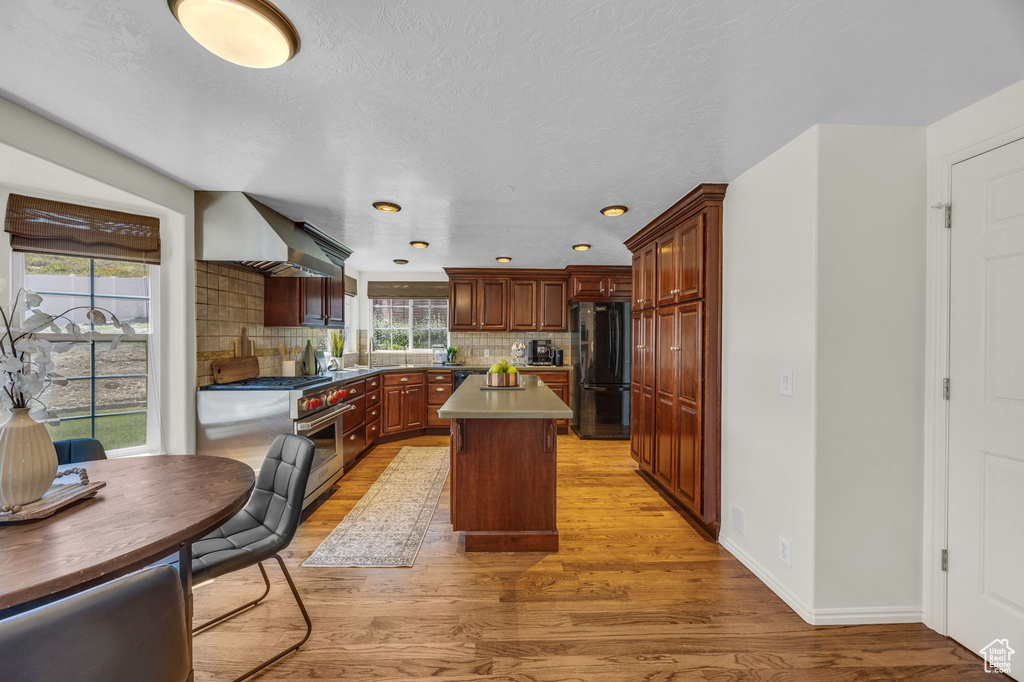 Kitchen with freestanding refrigerator, luxury stove, wall chimney range hood, tasteful backsplash, and light wood-style flooring