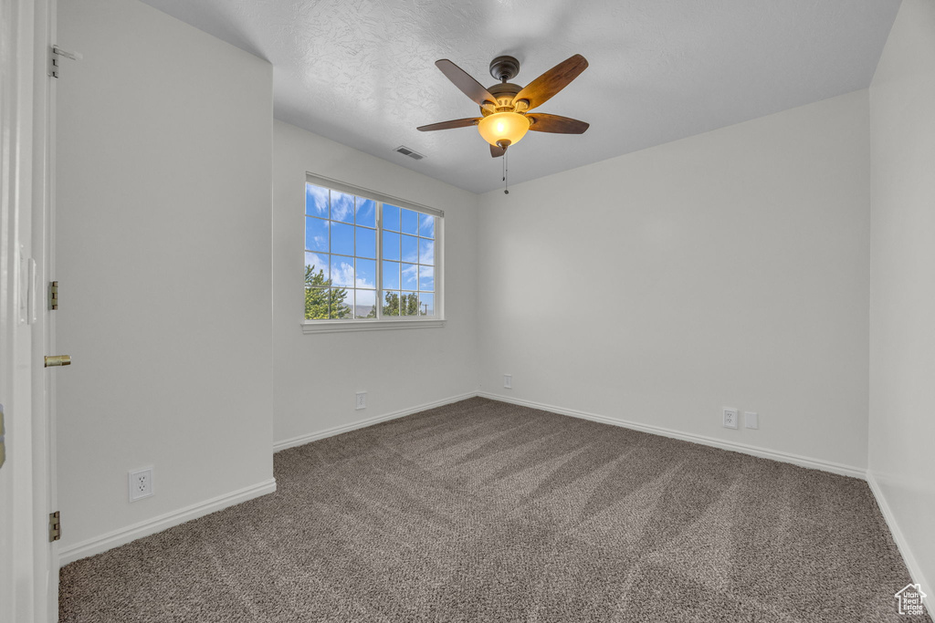 Empty room with dark carpet, baseboards, and ceiling fan