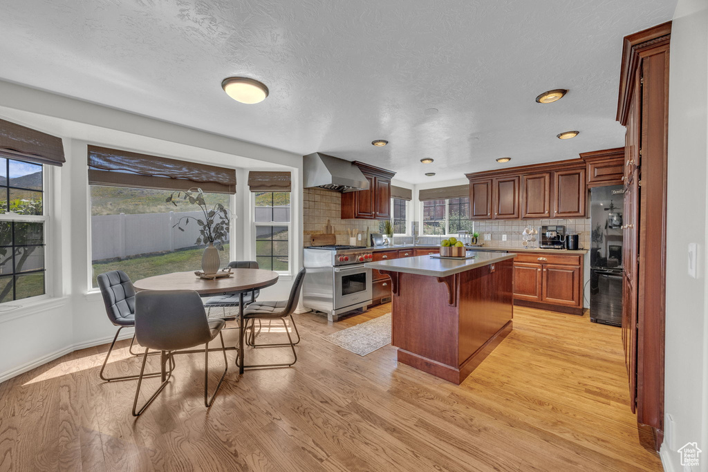 Kitchen featuring luxury stove, freestanding refrigerator, wall chimney range hood, plenty of natural light, and recessed lighting
