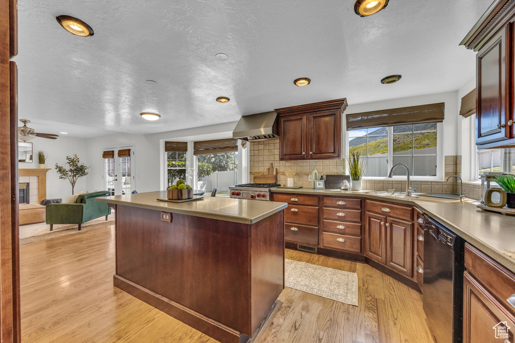 Kitchen with black dishwasher, light wood-style flooring, decorative backsplash, wall chimney exhaust hood, and a textured ceiling