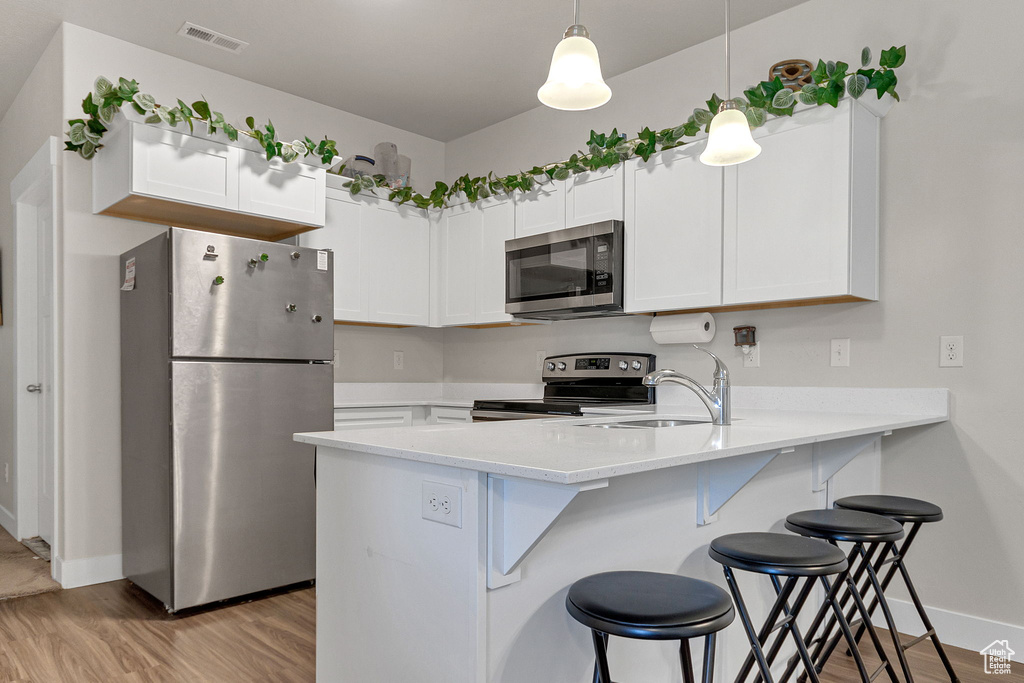 Kitchen with stainless steel appliances, a peninsula, light wood-style floors, a kitchen bar, and baseboards
