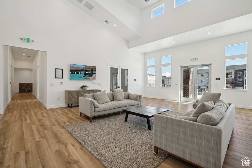 Living area with a towering ceiling, light wood-type flooring, plenty of natural light, baseboards, and recessed lighting