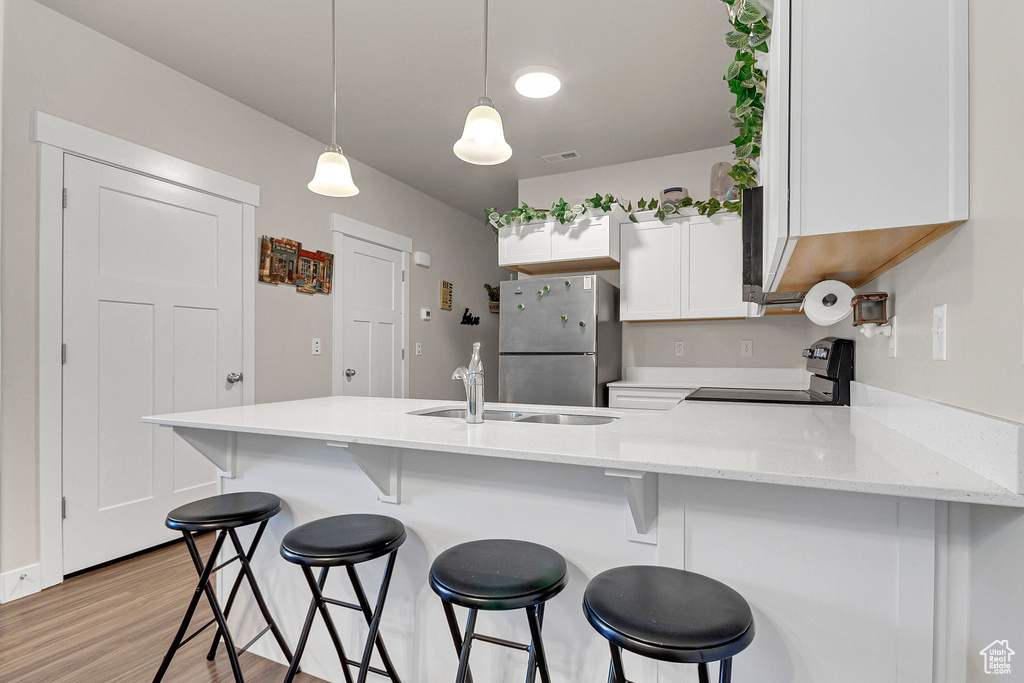 Kitchen with electric range oven, freestanding refrigerator, a sink, light wood-type flooring, and a peninsula