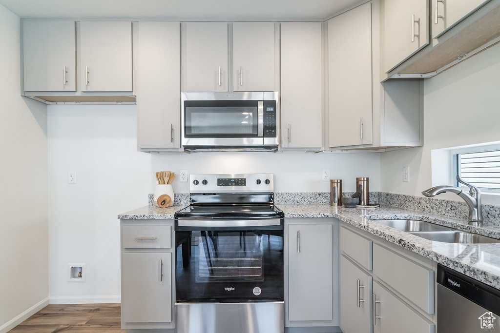 Kitchen featuring appliances with stainless steel finishes, wood finished floors, and light stone countertops
