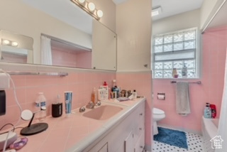 Bathroom featuring double vanity, toilet, tile walls, and shower / bathtub combination with curtain