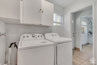 Laundry room featuring cabinet space, independent washer and dryer, light tile patterned floors, and baseboards