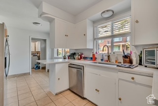 Kitchen with appliances with stainless steel finishes, light countertops, light tile patterned floors, white cabinets, and a peninsula