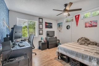 Bedroom featuring multiple windows, wood finished floors, a desk, and a ceiling fan