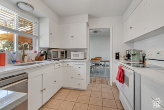 Kitchen with white appliances, a sink, light tile patterned flooring, and white cabinetry