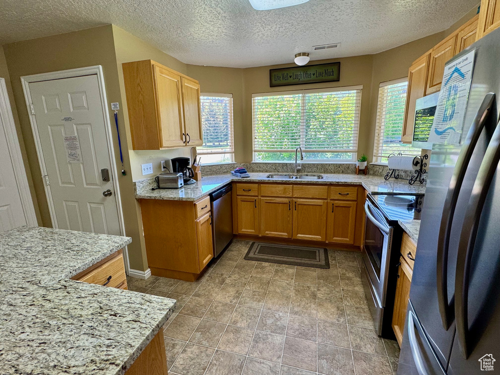 Kitchen with stainless steel appliances, a textured ceiling, and light stone countertops
