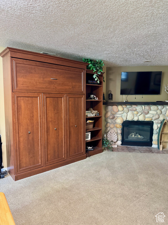 Unfurnished living room featuring carpet, a stone fireplace, and a textured ceiling