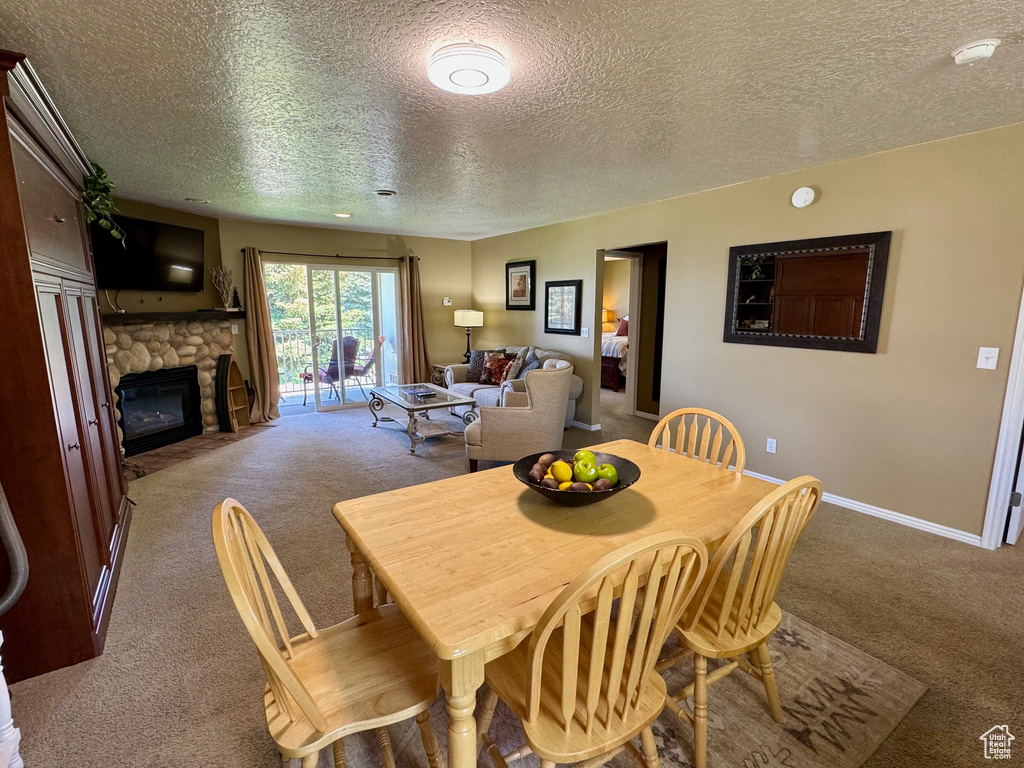 Dining area with carpet, a textured ceiling, and a stone fireplace