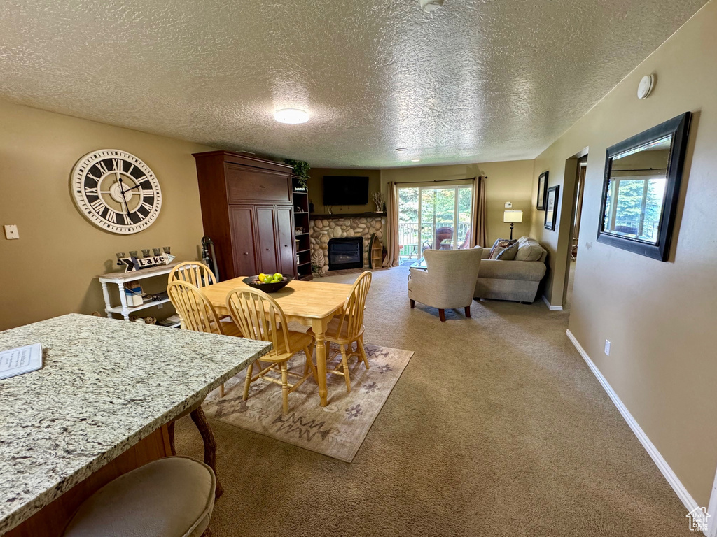 Dining room with a textured ceiling, a stone fireplace, and light carpet