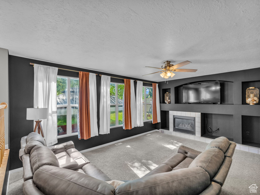 Living room featuring a textured ceiling, ceiling fan, baseboards, a fireplace, and carpet flooring