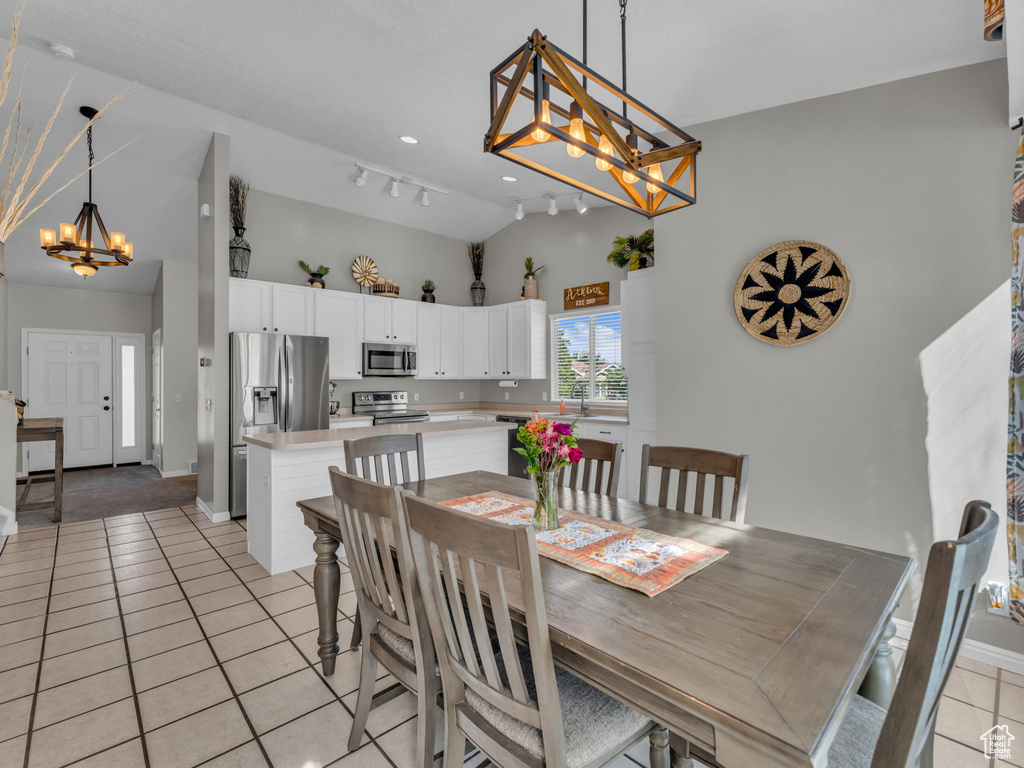 Dining space featuring a chandelier, light tile patterned flooring, track lighting, baseboards, and lofted ceiling
