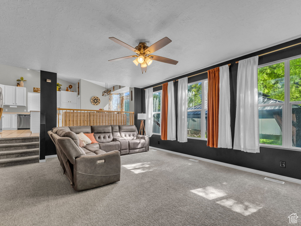 Carpeted living room featuring healthy amount of natural light, ceiling fan, a textured ceiling, baseboards, and lofted ceiling