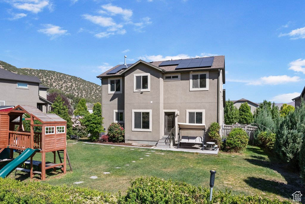 Back of house featuring a playground, stucco siding, solar panels, and a patio area