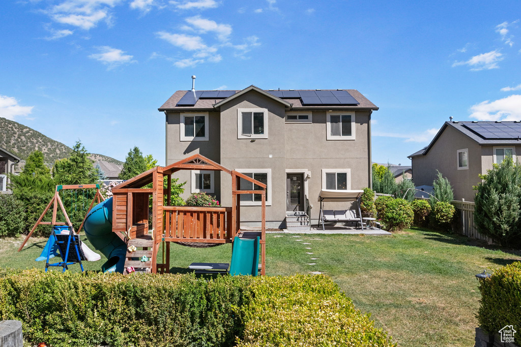 Back of house featuring stucco siding, a playground, roof mounted solar panels, and a patio area