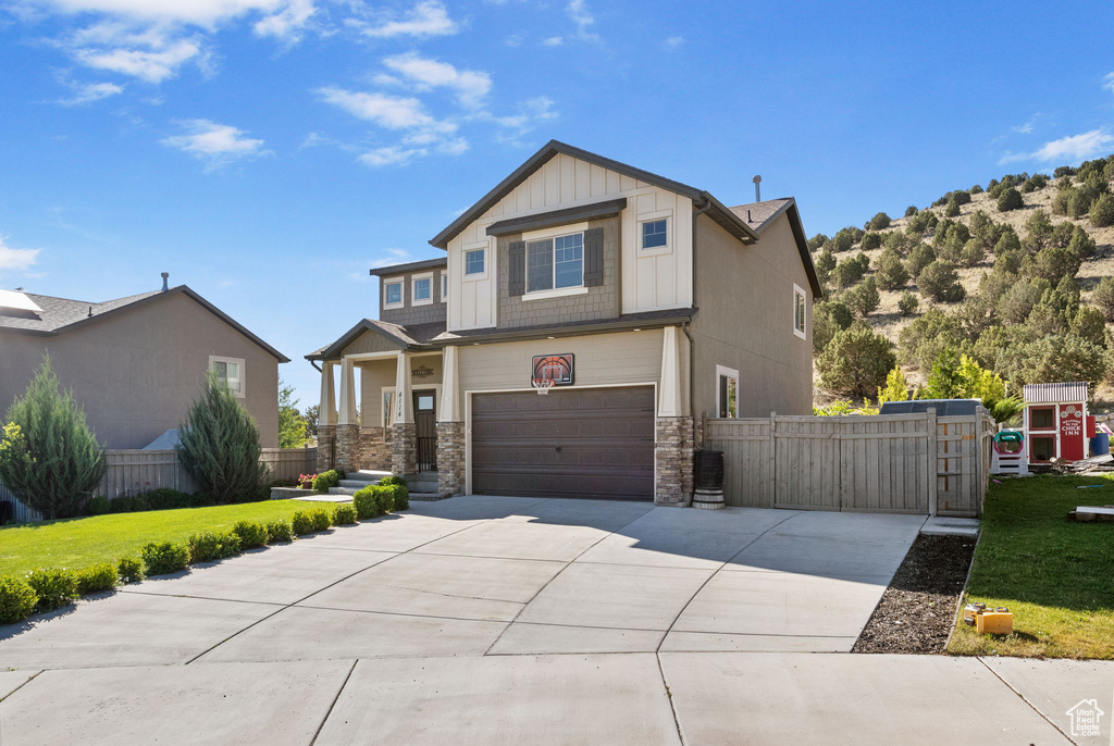 Craftsman house featuring stone siding, board and batten siding, concrete driveway, an attached garage, and a gate