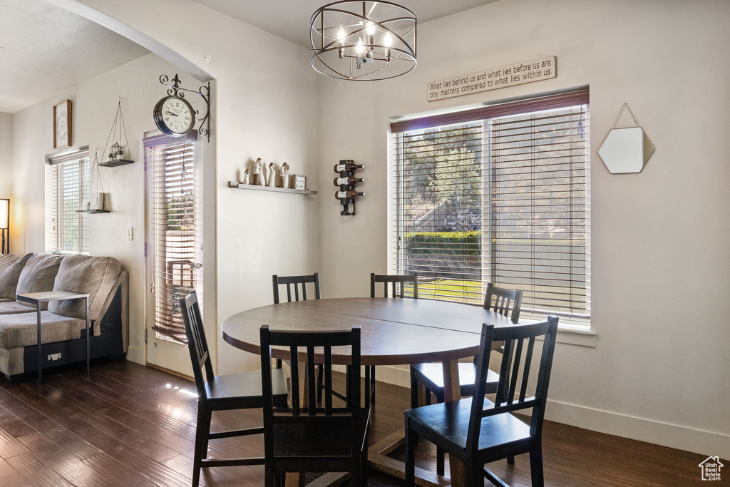 Dining space featuring dark wood-style floors, a chandelier, baseboards, and arched walkways