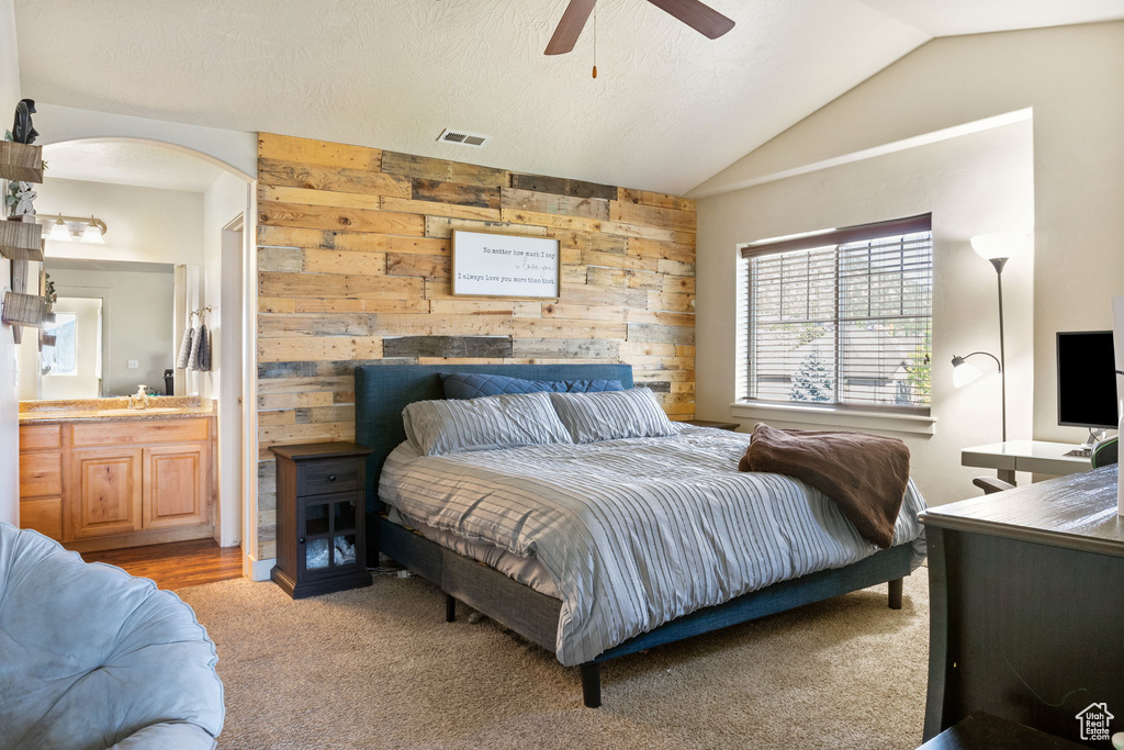 Carpeted bedroom featuring wooden walls, vaulted ceiling, connected bathroom, a ceiling fan, and a sink