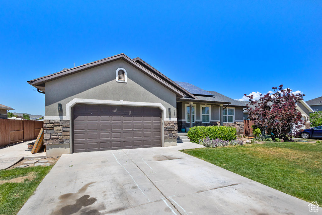 Single story home featuring stone siding, an attached garage, stucco siding, and roof mounted solar panels
