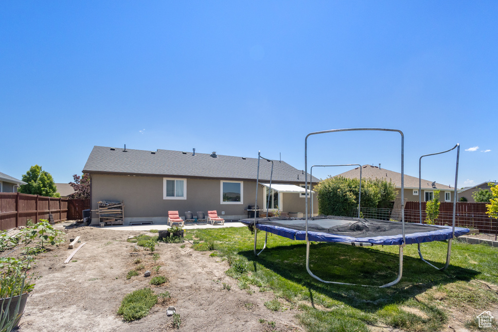 Rear view of property featuring a trampoline, a patio area, and stucco siding
