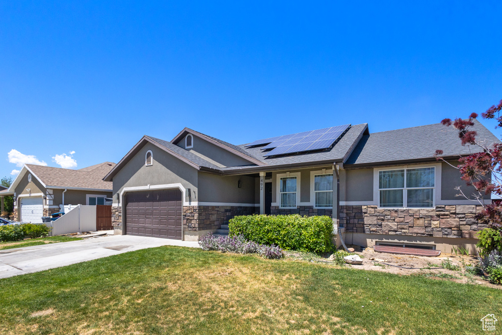 Ranch-style home featuring stucco siding, stone siding, roof mounted solar panels, and a garage