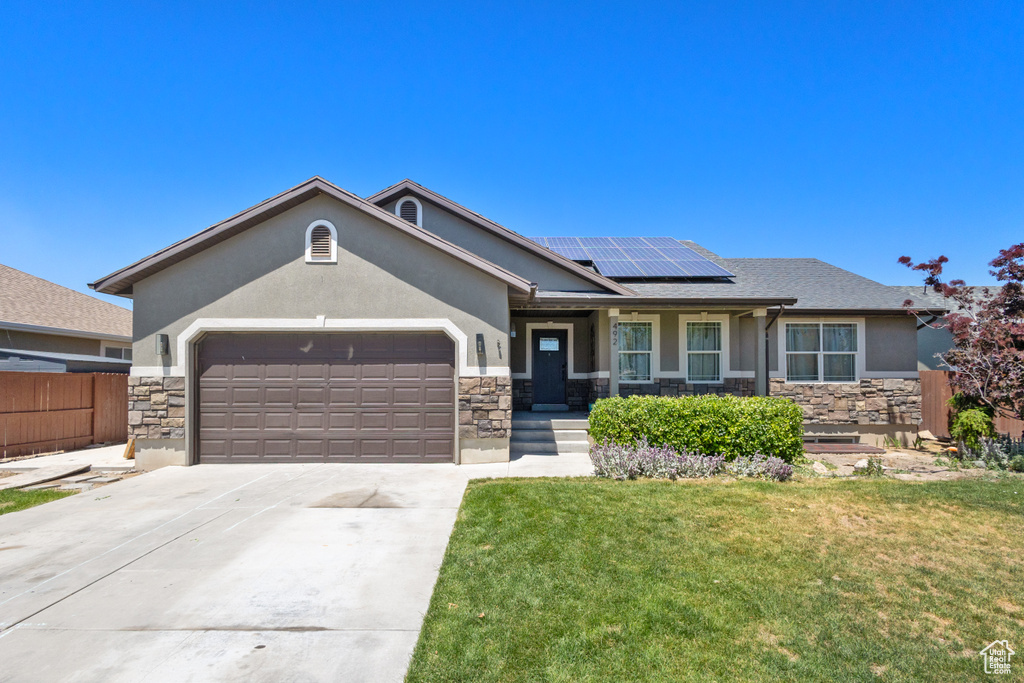 Ranch-style house with stone siding, stucco siding, a garage, and solar panels