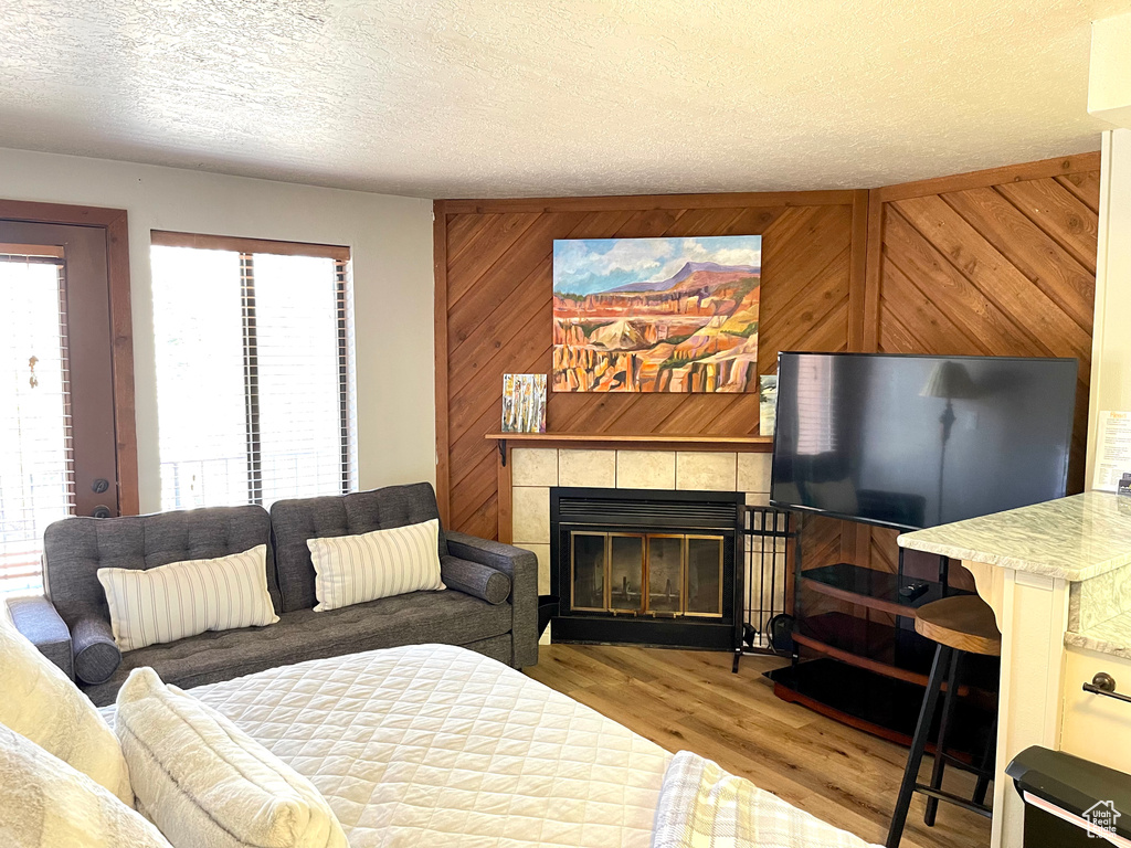 Living room with plenty of natural light, a tile fireplace, wood finished floors, a textured ceiling, and wood walls