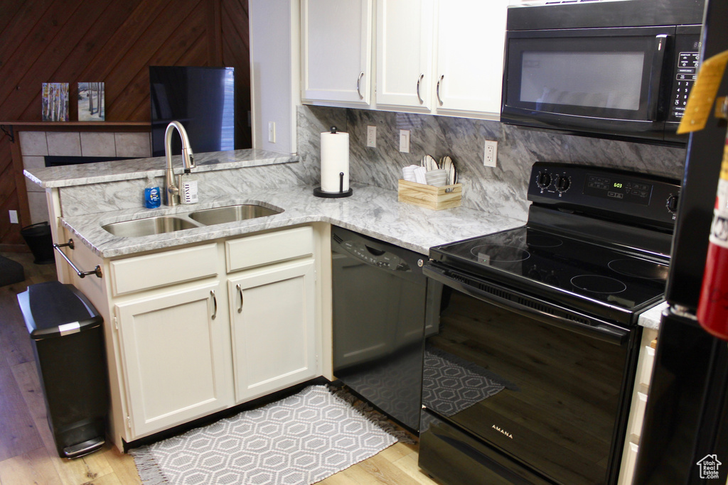Kitchen featuring black appliances, a sink, light wood-style flooring, backsplash, and light stone counters