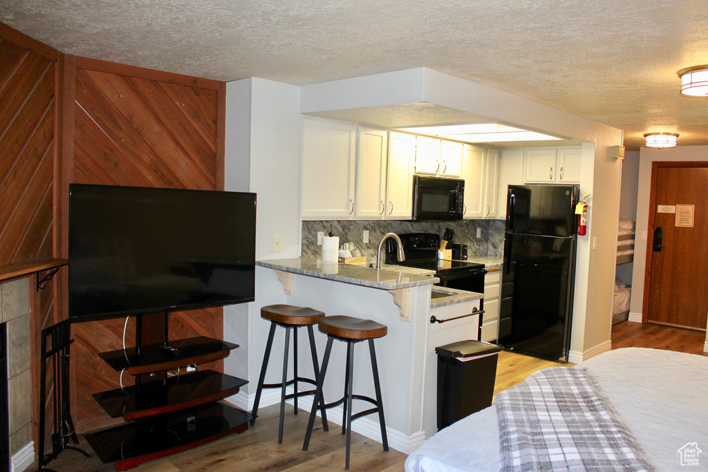 Kitchen with black appliances, backsplash, light wood finished floors, white cabinets, and a textured ceiling